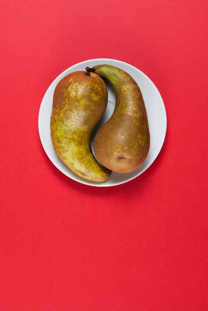 Two green pears on a white plate over red background. - Фото, изображение