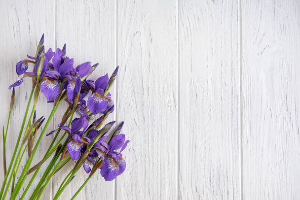 Achtergrond voor een spandoek met een boeket irissen op een lichte houten achtergrond. De basis voor het spandoek met bloemen. Blanco wenskaart. Uitzicht van bovenaf - Foto, afbeelding