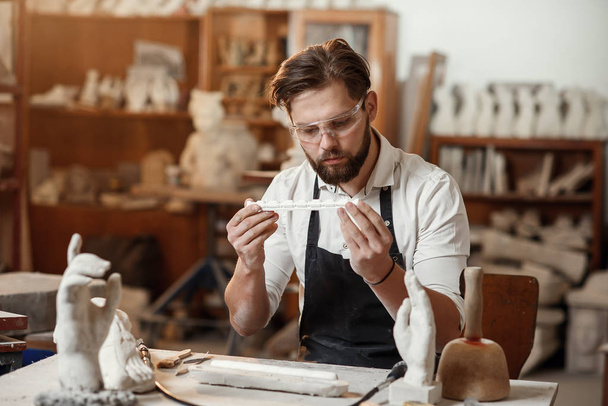 Concentrated sculptor with beard works in his workshop and looking at the ready gypsum decorative detail. - Photo, Image