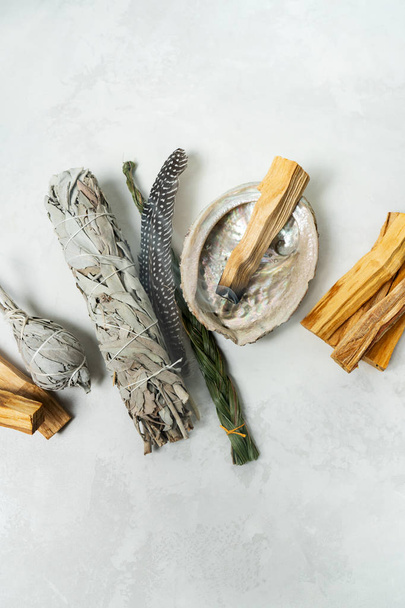 Smudge kit for spiritual practices with natural elements: Palo Santo sticks, dried white sage, Guinea Fowl feather, crystals, sea pearl shell Abalone on a light background. Balancing the soul. - Foto, Imagem