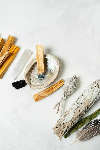 Smudge kit for spiritual practices with natural elements: Palo Santo sticks, dried white sage, Guinea Fowl feather, crystals, sea pearl shell Abalone on a light background. Balancing the soul. - Foto, imagen