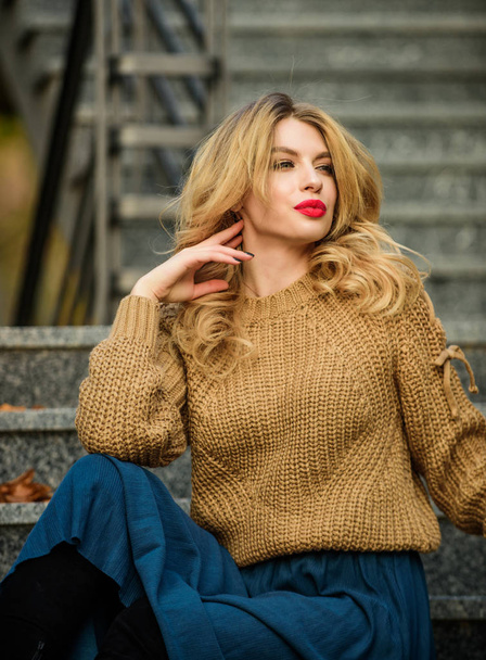 Warm autumn. Fall fashion trend. Wearable trends. Layer oversize knit over girly skirt. Woman gorgeous hairstyle sit on stairs outdoors. Fall outfit formula. Style Sweater and Skirt Combo for Fall - Zdjęcie, obraz