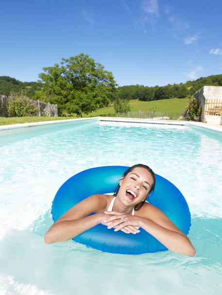Woman floating in inner tube in pool and laughing. Vertical - 写真・画像