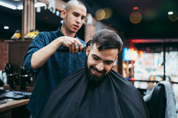 Good looking young adult man getting a hair and beard styling and dressing treatment by professional hairstylist. - Φωτογραφία, εικόνα