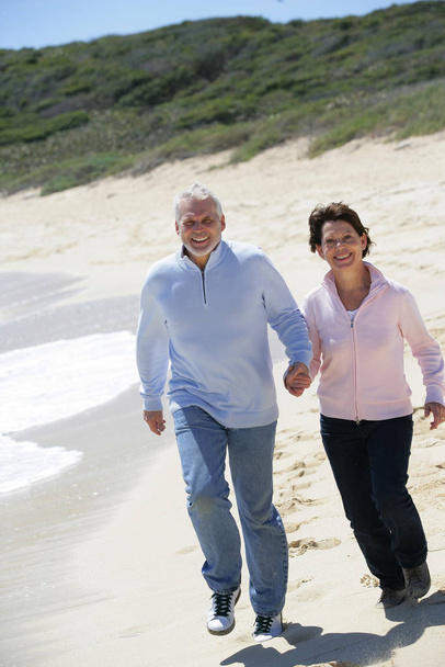 Smiling elderly couple walking along the beach holding hands - Fotoğraf, Görsel