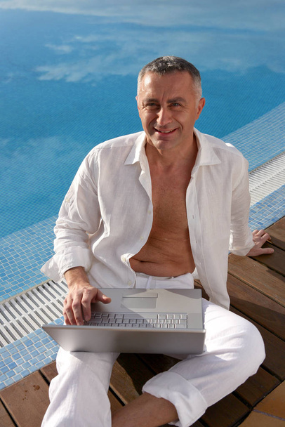 portrait of smiling man with laptop sitting on the edge of a pool side - Fotoğraf, Görsel