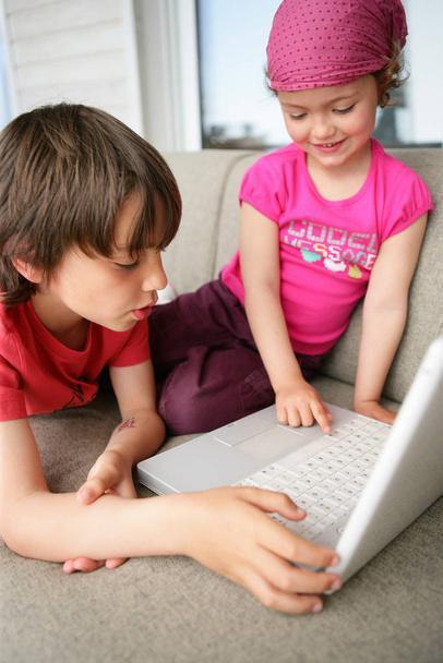 Portrait of a boy and a girl on a couch in front of a laptop - Фото, изображение