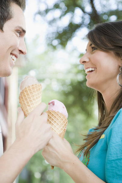 A young couple is eating ice cream together.  They are smiling at each other.  Vertically framed shot. - Foto, Bild