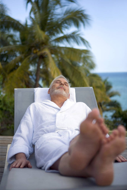 Elderly man in bathrobe lying on a sunbed - 写真・画像