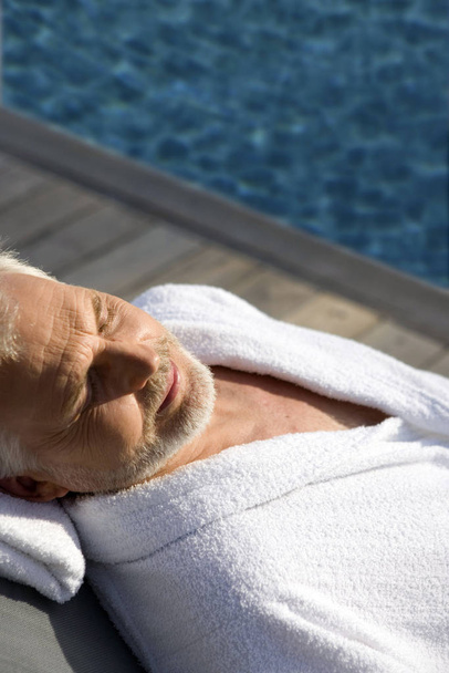 Old man lying on a lounge chair beside a swimming pool - Foto, imagen