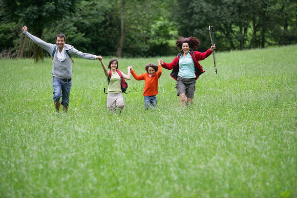 Man and woman with children running in the grass by raising his arms in the coun - 写真・画像