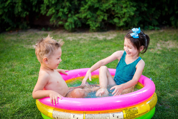 Deux petits frères et sœurs jouant et éclaboussant dans la piscine pendant la chaude journée d'été. Enfants nageant dans la piscine pour enfants. Deux joyeux enfants mignons jouent et s'amusent, éclaboussent dans la piscine gonflable à l'arrière-cour
 - Photo, image