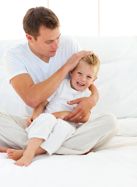 Adorable little boy having fun with his dad on a bed  - Fotó, kép