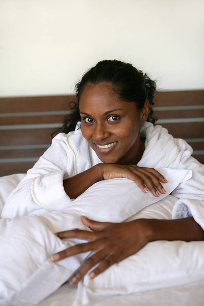 Portrait of a young Mtis woman in bathrobe smiling lying on bed  - Foto, afbeelding