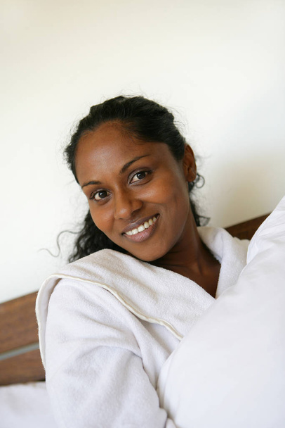 Portrait of a young Mtis woman in bathrobe smiling lying on bed  - Foto, Bild