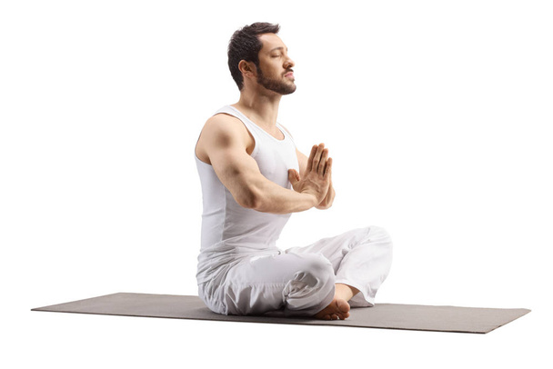 Young man sitting on an exercise mat in a meditation pose  - Fotó, kép