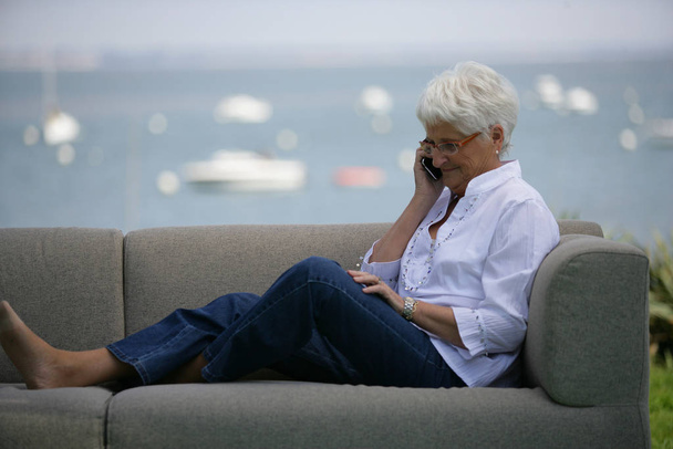 Senior woman sitting on a sofa with mobile phone - Foto, Bild