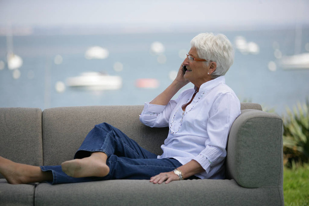 Mujer mayor sentada en un sofá con teléfono móvil - Foto, Imagen