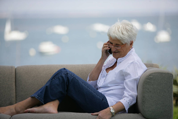 Senior woman sitting on a sofa with mobile phone - Foto, Bild