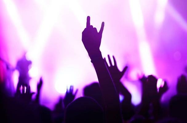 Publikum mit erhobenen Händen bei einem Musikfestival und Lichtern, die von der Bühne herabströmen. Publikum hebt die Hände, tanzt und genießt das Konzert. - Foto, Bild