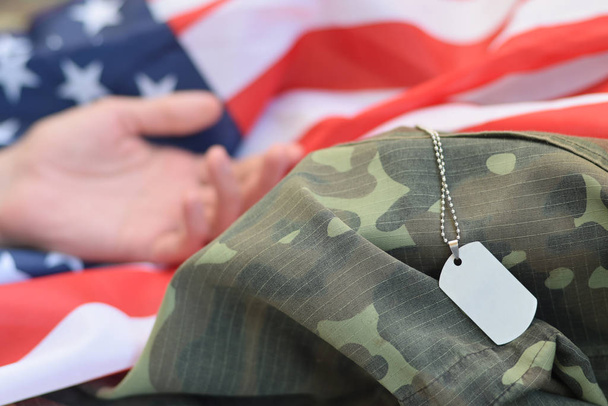 silberfarbene Militärperlen mit Hundeanhänger und der Hand eines toten Soldaten auf einer Stofffahne und Tarnuniform der Vereinigten Staaten - Foto, Bild