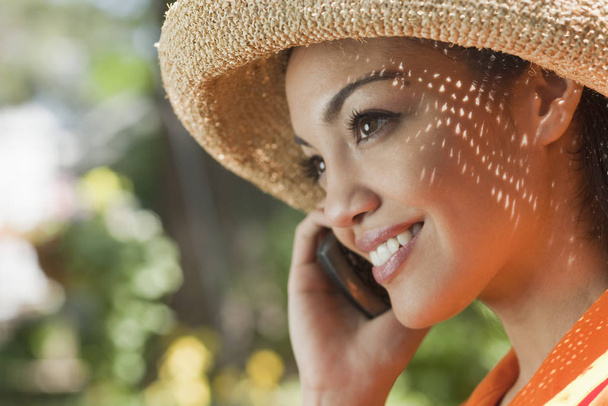 Close-up side view of a smiling young woman using a cell phone in an outdoor setting. Horizontal format. - Photo, image