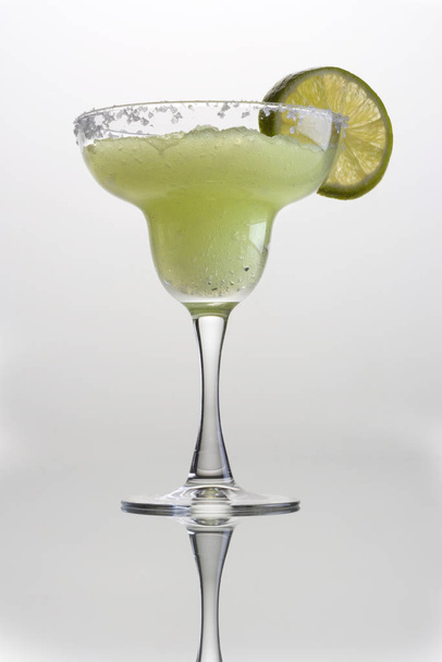 Frozen Margarita mixed drink with lime slice garnish on plain grey background with reflection - Foto, afbeelding