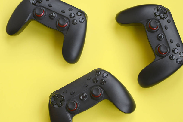 Tres modernos mandos negros sobre fondo amarillo. Permite jugar videojuegos junto con el concepto de amigos. Trabajo en equipo cooperativo
 - Foto, imagen