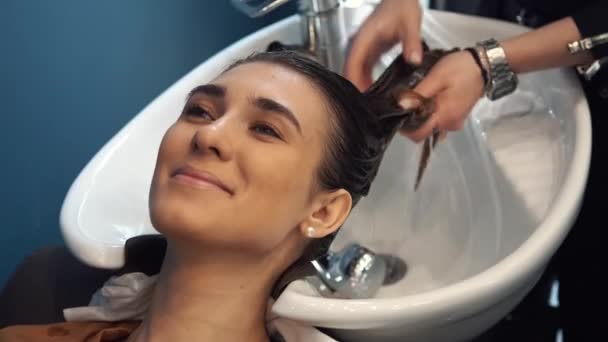 Schönheits-, Haarpflege- und People-Konzept - glückliche junge Frau mit Friseurwaschkopf im Friseursalon - Filmmaterial, Video