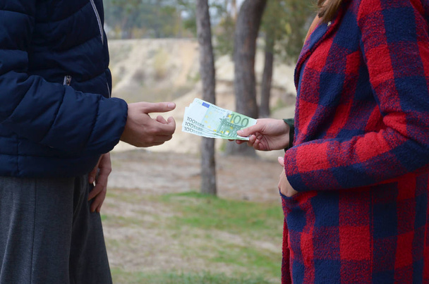 Une fille transfère des billets d'euros aux mains d'un jeune homme en forêt. Concept de vol qualifié ou de transaction illégale
 - Photo, image