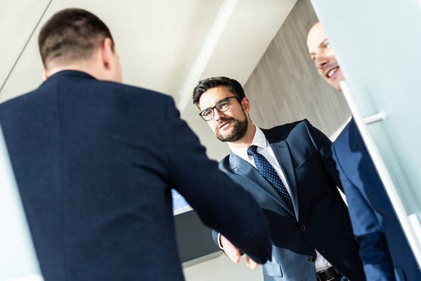 近代的なオフィスでのビジネスミーティングで握手を交わしたり、握手を交わして契約を締結することで、自信を持ってビジネスの人々のグループ. - 写真・画像