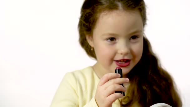A little girl does makeup in front of a small mirror. Close-up on a white background - Footage, Video