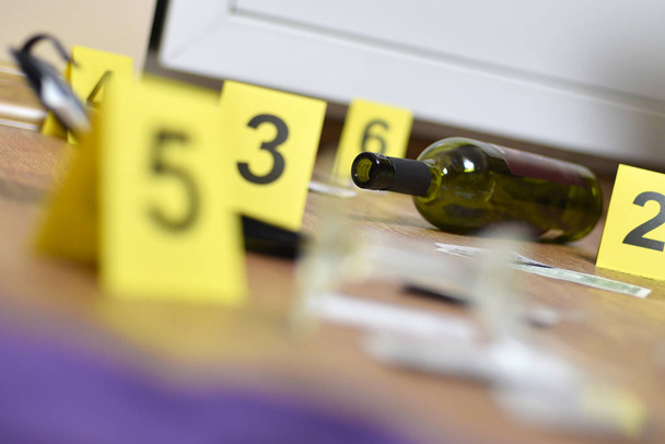 Broken glass and bottle of wine marked as evidence during crime scene investigation. Many yellow markers with numbers - Photo, Image