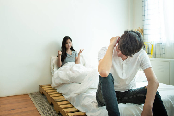 アジアの男は落ち込み、不幸な関係を持つ女性は議論を持っている後、ベッドの上に座って、カップルの社会問題が住んでいる. - 写真・画像