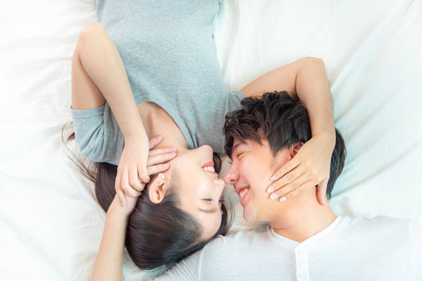 幸せな若いアジアのカップルの肖像画を閉じます。アジアの男性と女性は大きな笑顔の手のタッチ顔と一緒にベッドの上に横たわります,バレンタインコンセプトと愛の感情 .  - 写真・画像