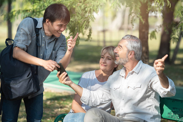азиатских туристов молодой человек со смартфоном в руках спрашивает дорогу у старого кавказского старейшины, который сидит с женщиной, он указал пальцем на то, как
. - Фото, изображение