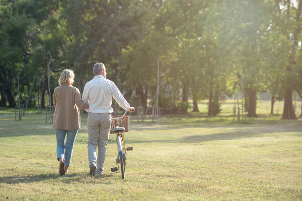 Ein fröhliches, aktives Seniorenpaar mit Fahrrad spaziert gemeinsam durch den Park. Perfekte Aktivitäten für ältere Menschen im Ruhestand. - Foto, Bild