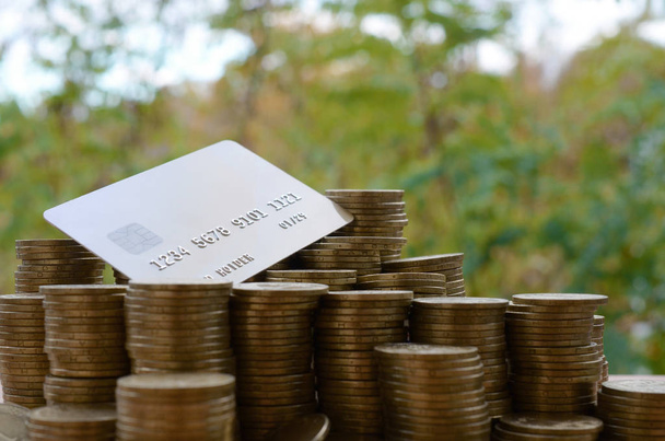 Karta kredytowa na dużej stercie błyszczących ukraińskich starych 1 hrywien stosy monet na rozmazanym tle zielonych drzew. Koncepcja przelewu i bankowości internetowej na Ukrainie - Zdjęcie, obraz