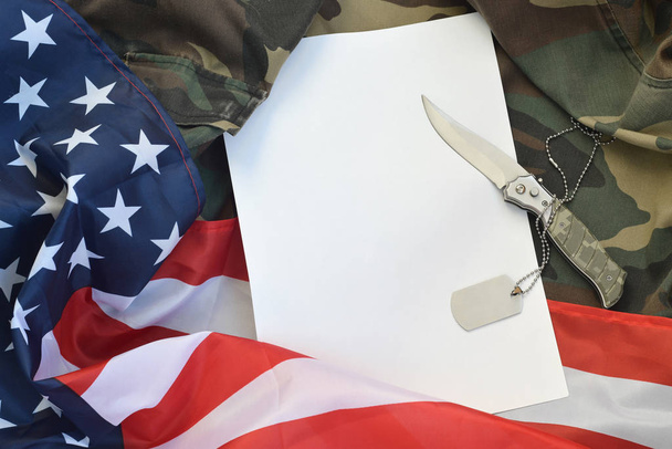 Pusty papier leży z nożem i naszyjnikiem nieśmiertelnika armii na mundurze kamuflażu i amerykańskiej fladze - Zdjęcie, obraz