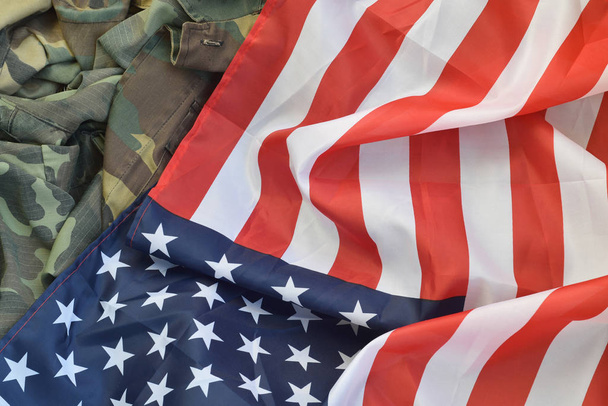 Σημαία Ηνωμένων Πολιτειών Αμερικής και διπλωμένο στρατιωτικό σακάκι. Στρατιωτικά σύμβολα εννοιολογικό πανό υπόβαθρο για αμερικανικές πατριωτικές διακοπές - Φωτογραφία, εικόνα