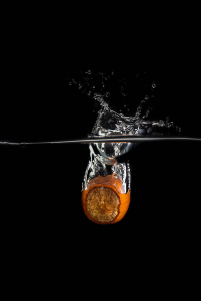 One hazelnut falls into the water with splashes and bubbles on a black background - Фото, зображення