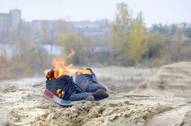 Des baskets de sport brûlantes ou des chaussures de sport sur le feu se dressent sur la côte sablonneuse de la plage. L'athlète a brûlé. Exercice physique pendant le concept d'entraînement
 - Photo, image