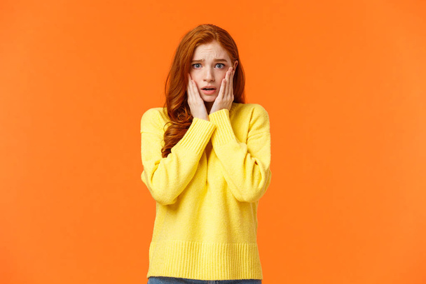 Concerned and anxious redhead girl forgot take chicken out freezer before mom came home, grab face, gasping scared and troubled, dont know what do, standing tensed and afraid, orange background - Фото, зображення