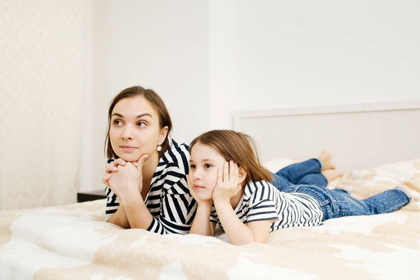Young mother and her daughter child lying on bed in bedroom and  - Photo, Image