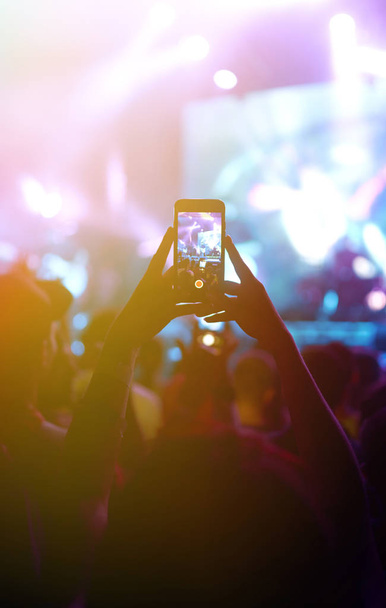 Kéz egy telefon rekordok élő zenei fesztivál. Az emberek okostelefonnal fényképeznek egy nyilvános zenei koncerten. A közönség felemeli a kezét, táncol és élvezi a koncertet.. - Fotó, kép