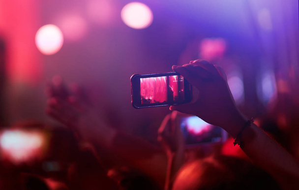 Mano con un teléfono graba el festival de música en vivo. Gente tomando fotografías con un teléfono inteligente durante un concierto de música pública. Multitud levantando las manos, bailando y disfrutando mucho del concierto
. - Foto, imagen