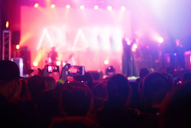 Hand met een telefoon neemt live muziek festival. Mensen die foto 's maken met een smartphone tijdens een publiek muziekconcert. Het publiek steekt zijn hand op, danst en geniet van het concert. - Foto, afbeelding