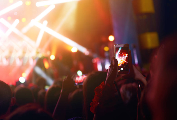 Kéz egy telefon rekordok élő zenei fesztivál. Az emberek okostelefonnal fényképeznek egy nyilvános zenei koncerten. A közönség felemeli a kezét, táncol és élvezi a koncertet.. - Fotó, kép