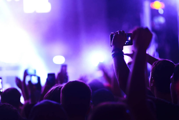 Hand mit einem Telefon Platten Live-Musik-Festival. Menschen, die während eines öffentlichen Musikkonzerts mit dem Smartphone Fotos machen. Publikum hebt die Hände, tanzt und genießt das Konzert. - Foto, Bild