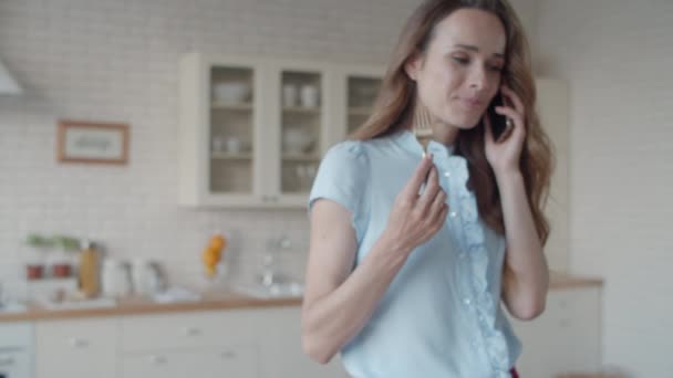 Young businesswoman talking mobile phone in white kitchen interior. - Video, Çekim